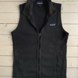 Svart fleeceväst från Patagonia - Säljer en svart fleeceväst från Patagonia med dragkedja framtill. Västen har en hög krage och två fickor med dragkedja. Perfekt för lager-på-lager under kyliga dagar.