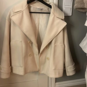 Kappa ifrån DesignBySi - Snygg beige kappa från Zara med dubbelknäppning och breda slag. Jackan har en kortare passform och stora fickor framtill. Perfekt för en stilren look.