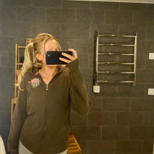 Brun hoodie från Peak Performance - Säljer en brun hoodie från Peak Performance med rosa detaljer och dragkedja. Tröjan är i storlek L men sitter perfekt på mig som vanligtvis har S. Den har några små fläckar på ärmarna men syns knappt. 