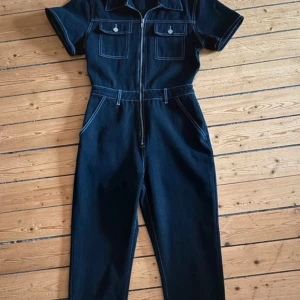 Svart jeans jumpsuit från Boohoo - Snygg svart jeans jumpsuit från Boohoo med korta ärmar och dragkedja framtill. Den har två bröstfickor, framfickor och två bakfickor. Endast testad då den är köpt på Vinted, men passade inte mig.