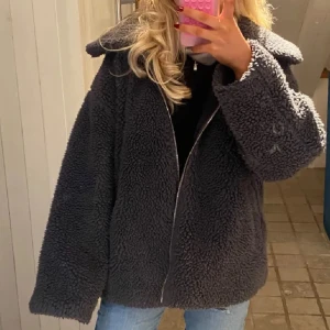 Grå teddyjacka med dragkedja - Mysig grå teddyjacka med dragkedja framtill. Perfekt för kyliga dagar med sin fluffiga och varma design. Har en lite mer overzised passform