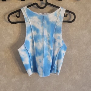 Blå och vit ribbad linnetopp från FB Sister - Snygg blå och vit ribbad linnetopp från FB Sister med ett molnliknande mönster. Perfekt för en avslappnad stil. Toppen är ärmlös och har en bekväm passform.