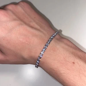 Glittrande tennis armband i silver - Snyggt och elegant armband i silver med gnistrande stenar. Perfekt för att ge en touch av glamour till din stil. Armbandet har en säker låsning och är lätt att bära.