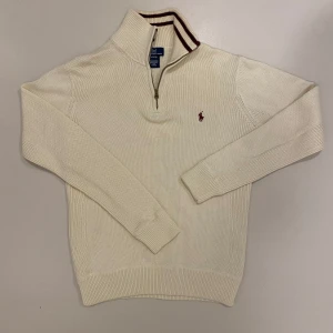 Stickad Ralph lauren halv zip - Säljer en stilren vit stickad halv zip från Polo Ralph Lauren i barn storlek L så den passar ungefär som en vanlig S. använd Max 3 gånger, Tröjan har en halv dragkedja och en broderad logotyp på bröstet. Tillverkad i mjuk bomull med ribbade muddar och krage. Skriv vid minsta fråga eller fundering🔥👍