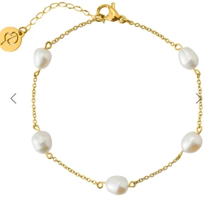 Guldarmband med pärlor - Elegant guldarmband med fem vita pärlor jämnt fördelade längs kedjan. Armbandet har en justerbar kedja med ett litet hjärthänge. Perfekt för att ge en sofistikerad touch till din stil.