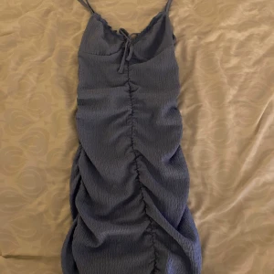 Blå klänning med knyt - Snygg blå klänning med smala axelband och knyt framtill. Den har en rynkad design som ger en fin struktur och form. Perfekt för en somrig look.