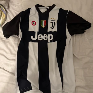 Juventus fotbollströja med Ronaldo 7 - Snygg Juventus fotbollströja med Ronaldo 7 på ryggen. Tröjan är randig i svart och vit med korta ärmar och sponsorlogga på framsidan. Perfekt för fans av laget och spelaren!