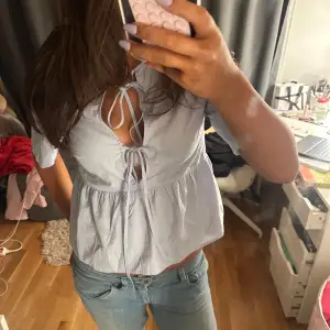 Säljer en söt ljusblå blus med knytning framtill och v-ringad design. Blusen har korta ärmar och en luftig passform, perfekt för varmare dagar. Passar bra till både jeans och kjol.