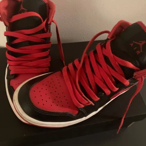 Nike Air Jordans i rött och svart - Snygga Nike Air Jordans i rött och svart med klassisk design. Skorna har en hög modell med snörning och en slitstark sula. Perfekta för dig som vill ha en stilren och sportig look.kommer även med svarta skosnören separat.storlek 40,5