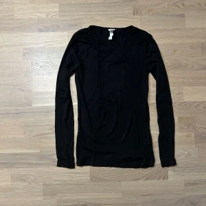 Svart ribbad tröja från H&M - Säljer en stilren svart ribbad tröja från H&M. Tröjan har långa ärmar och en rund halsringning, perfekt för lager-på-lager under kyligare dagar.