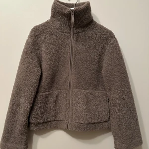Brun teddyjacka med dragkedja - Mysig brun teddyjacka med hög krage och dragkedja framtill. Jackan har långa ärmar och två fickor. Den är väldigt lite använd och känns som ny och fräsch. 200kr+frakt