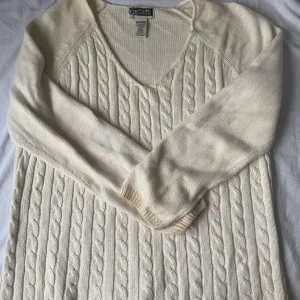 Vit stickad tröja från Route 66 - Säljer en mysig vit stickad tröja från Route 66. Tröjan har ett klassiskt flätmönster och en v-ringad hals. Perfekt för kyliga dagar. Tillverkad i en bomulls- och akrylblandning.