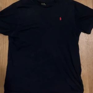 Ralph lauren t-shirt - Svart Ralph Lauren t-shirt med det klassiska märket på bröstet. Den är i bra skick och jag säljer för att den inte används längre. Skriv vid frågor! Priset inte hugget i sten.