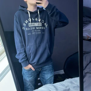Mörkblå hoodie från Jack & Jones - Säljer en snygg mörkblå hoodie från Jack & Jones i storlek L. Modellen på bilden är 167cm lång så skulle säga att den är rätt så liten i storleken. Skick 8/10 använd men i gott skick. Skriv om du funderar över något!