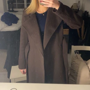 Brun kappa med bälte - Säljer en elegant brun kappa med bälte och långa ärmar. Perfekt för höst och vinter, med en klassisk design som passar till många tillfällen.