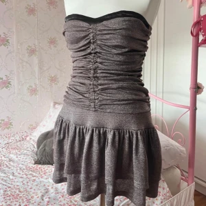 Glittrig axelbandslös klänning - Snygg glittrig axelbandslös klänning med rynkade detaljer och volangkjol. Perfekt till nyår, skickar snabbt så den hinner komma fram. Märket är I am Gia