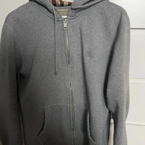 Grå burberry zip hoodie - Säljer nu min butberry zip hoodie, tröjan är använd sparsamt och är strl L men passa på M.