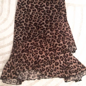 Leopardmönstrad kjol med volang - Snygg leopardmönstrad kjol med volangdetaljer. Perfekt för att ge en vild touch till din outfit. Kjolen har en flödande design som ger en fin rörelse.