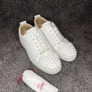 Christian Louboutin skor - Snygga vita sneakers från Christian Louboutin med nitar på tån och den ikoniska röda sulan. Skorna har snörning och är tillverkade i skinn, vilket ger en lyxig känsla. Bra skick och pris kan givetvis diskuteras. Påse tillkommer vid köp och äkthetsbevis finns. Bara att höra av sig vid frågor!