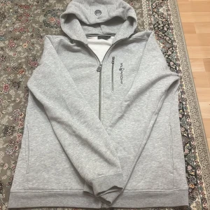  Säljer en stilren grå sail racing kofta - Säljer en stilren grå hoodie från sail racing med dragkedja och justerbar huva. Perfekt för kyliga dagar och avslappnade stunder. Den har långa ärmar och en diskret logga på bröstet.