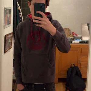 Mörkbrun identity hoodie med rött tryck - Tja! Säljer en mörkgrå hoodie med en stor röd logga på framsidan. Hoodien har en röd insida i huvan och matchande röda snören. Säljer tröjan då den blivit för liten för mig men den är fortfarande i bra skick. Perfekt för en avslappnad stil. 