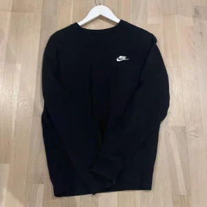 Svart tröja från Nike - Säljer en stilren svart tröja från Nike med deras fina logga på bröstet. Tröjan har långa ärmar och en klassisk rund halsringning. Perfekt för en avslappnad look. Perfekt skick och väldigt skön