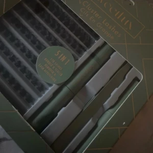 Cluster Lashes 5-i-1 - Förpackning med 5-i-1 cluster lashes för att skapa fylliga och dramatiska fransar. Innehåller flera rader av fransar och två applikatorer i en elegant grön förpackning.