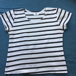 Randig topp från Calvin Klein - Säljer en stilren randig topp från Calvin Klein i svart och vit. Toppen har korta ärmar och en rund halsringning. Perfekt för en avslappnad look.