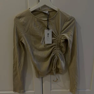 Beige ribbad topp från NA-KD - Snygg beige ribbad topp från NA-KD med lång ärm och rynkdetalj på sidan. Perfekt för en stilren look. Toppen är i ett hållbart material och har en rund halsringning.