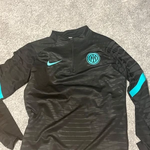 Svart Dri-FIT  tröja från Nike - Snygg svart tröja från Nike med Dri-FIT ADV-teknologi. Tröjan har ett stilrent mönster och Inter-logga i turkos på bröstet. Perfekt för fotbollsträning eller som en sportig vardagströja Denna är köpt i Italien och går knappast att hitta någon i Sverige..