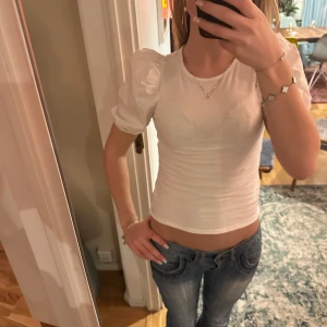 Vit kortärmad topp från H&M - Säljer en söt vit topp från H&M med puffiga korta ärmar. Toppen är i mjukt bomullsmaterial och har en rund halsringning. Använd en gång!