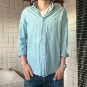 Ljusblå skjorta från Ralph Lauren - Snygg ljusblå skjorta från Ralph Lauren med klassisk krage och knappar framtill. Perfekt för en stilren look. Skjortan är i 9/10 skick, använts ett få antal gånger.