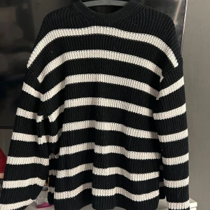 Svart & vit randig stickad tröja - Säljer en mysig svart och vit randig stickad tröja med långa ärmar. Tröjan har en loose passform och är perfekt för kyligare dagar. Den har en klassisk rund hals och ribbade kanter.