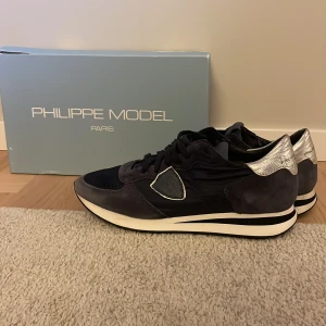 Philippe Model Trainers  - Snygga Philippe Model sneakers i svart med silverdetaljer. Skorna har en klassisk design med snörning och en bekväm sula. Storlek 39 men passar 40!! Skicket på skorna är 9/10. Pris kan diskuteras och skriv om ni har några funderingar!!