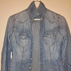 Blå jeansjacka från H&M - Snygg blå jeansjacka från H&M med klassisk design och knappar framtill. Garderobsrensning så kika gärna på övriga auktioner.