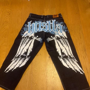 BAGGY JEANS med tryck  - Unika baggy jeans med stort vitt och blått tryck på baksidan. Byxorna har en väldigt väldigt baggy och loose passform och är perfekta för någon som gillar skate stil. Byxorna går att få en lågmidjad design om man viker ner de. De har väldigt bra material. Jag har använt de fem gånger. Tvättats en gång och har nu bestämt mig för att sälja de. Byxorna ser helt nya ut så de är verkligen i topp skick. Köpte de för 1400 kronor. Storlek 42. Vill sälja byxorna så snabbt som möjligt så hör gärna av dig