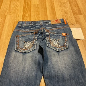 Lågmidjade bootcut jeans med specialfickor  - (19) världens snyggaste ljusblåa jeans med massa snygga detaljer på fickor och framsida, helt nya med lappar kvar. Midjemått rakt över: ca 34 cm, innerbenslängd: ca 88cm. Gylfen har tyvärr hoppat ur kedjan går säkert att fixa💝