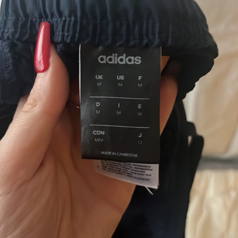 Snygga svarta träningsbyxor från Adidas med de klassiska tre vita ränderna längs sidorna. Byxorna har en elastisk midja med snörning för perfekt passform. Perfekta för träning eller en avslappnad dag.praselbyxor täck byxor . Farkut & Housut.