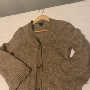 Beige stickad kofta - Mysig beige stickad kofta med knappar framtill. Perfekt för kyliga dagar med sin ribbade design vid ärmslut och nederkant. En klassisk och tidlös stil som passar till det mesta.