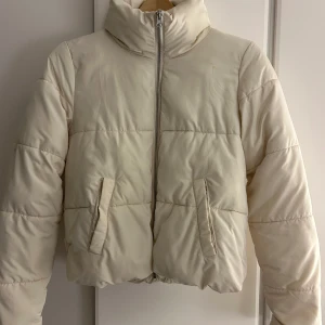 Vit pufferjacka från JDY - Säljer en stilren vit pufferjacka från JDY. Jackan har en dragkedja framtill och praktiska fickor. Perfekt för kyliga dagar med sin varma och bekväma design. Liten fläck fram som ev går bort, ej testat.