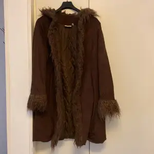 Snygg brun mocka kappa med quiltat foder och fluffiga pälsdetaljer på huva, ärmslut och framkant. Perfekt för kyliga dagar när du vill hålla stilen. Kappan har en lång och elegant passform. I storlek 40 men passar  mig som har 38. 