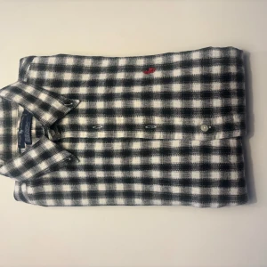 Rutig skjorta från Ralph Lauren - Snygg rutig skjorta från Ralph Lauren i svart och vit med en liten röd broderad logga på bröstet. Perfekt för en stilren look! Hör av dig vid intresse!