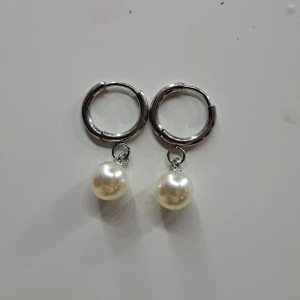 Silverfärgade örhängen med pärlor - Snygga silverfärgade örhängen med hängande vita pärlor. Perfekta för att ge en elegant touch till din outfit. De har en enkel och stilren design som passar till många tillfällen. PRISET KAN DISKUTERAS