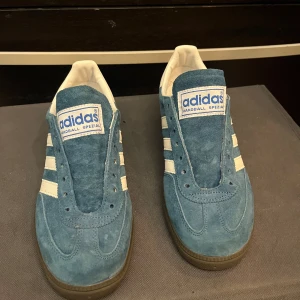 Blå Adidas Spezial sneakers - Snygga blå Adidas Handball Spezial sneakers i mocka med vita detaljer och klassiska tre ränder på sidan. Skorna har en robust brun sula och Adidas-logga på hälen och plösen. Perfekta för en sportig look. Nya, Saknar snören och kartongen 