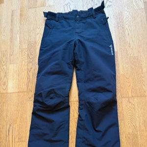 Svarta skidbyxor från Brunotti - Säljer ett par svarta skidbyxor från Brunotti. Byxorna har dragkedja och knappar i midjan samt justerbara remmar för bästa passform. Lätt utsvängda ben, passar över pjäxor. 