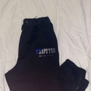 Svarta mjukisbyxor med broderi - Snygga svarta mjukisbyxor med broderad text på sidan. Perfekta för en avslappnad stil med elastisk midja och snörning. Byxorna har en bekväm passform och är gjorda i mjukt material.