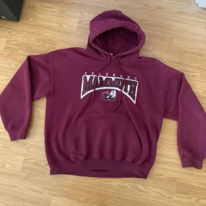 Vinröd Colorado Mammoth hoodie - Säljer en vinröd hoodie med Colorado Mammoth-tryck. Den har en klassisk känguruficka och en bekväm huva med dragsko. Perfekt för en avslappnad stil. Storleken är L men passar mer som en M
