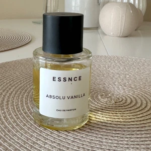 Essnce Absolu Vanilla Eau de Parfum - Säljer en flaska Essnce Absolu Vanilla Eau de Parfum. Doften har en varm och söt vaniljton. Flaskan är genomskinlig med en svart kork och en enkel, stilren etikett.