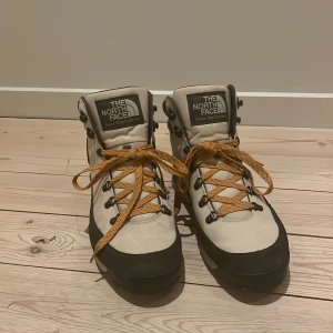 Beige och svarta kängor från The North Face - Säljer ett par robusta kängor från The North Face i beige och svart. Skorna har snörning och är perfekta för utomhusaktiviteter. De är tillverkade i slitstarkt material och har en bekväm passform. Anbända enstaka gånger så har lite tecken på användning nypris ligger på 1000kr