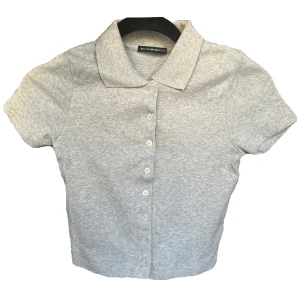 Grå croptop med krage Brandy Melville - Grå croptop med knappar och krage från Brandy Melville💕 aldrig använd! Storlek onesize, 100% bomull🩷